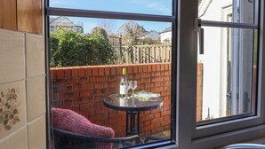 A view through a window of a brick wall, a round table with a bottle and glasses, and a red chair. - 4 Lymbrook Cottages (Lyme Regis)