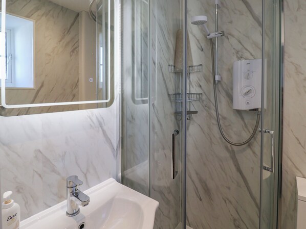Un baño moderno con ducha envuelta en vidrio, un lavabo blanco y un rebozado de mármol.