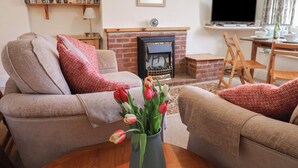 A cozy living room with a fireplace, a sofa, a coffee table with a vase of tulips, and a bookshelf. - 4 Lymbrook Cottages (Lyme Regis)