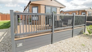 A modern caravan with a fenced deck, a gravel ground, and a clear sky. - Long Acres Lodge (Evesham)