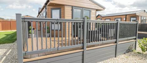 A modern caravan with a fenced deck, a gravel ground, and a clear sky.