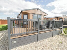 A modern caravan with a fenced deck, a gravel ground, and a clear sky.