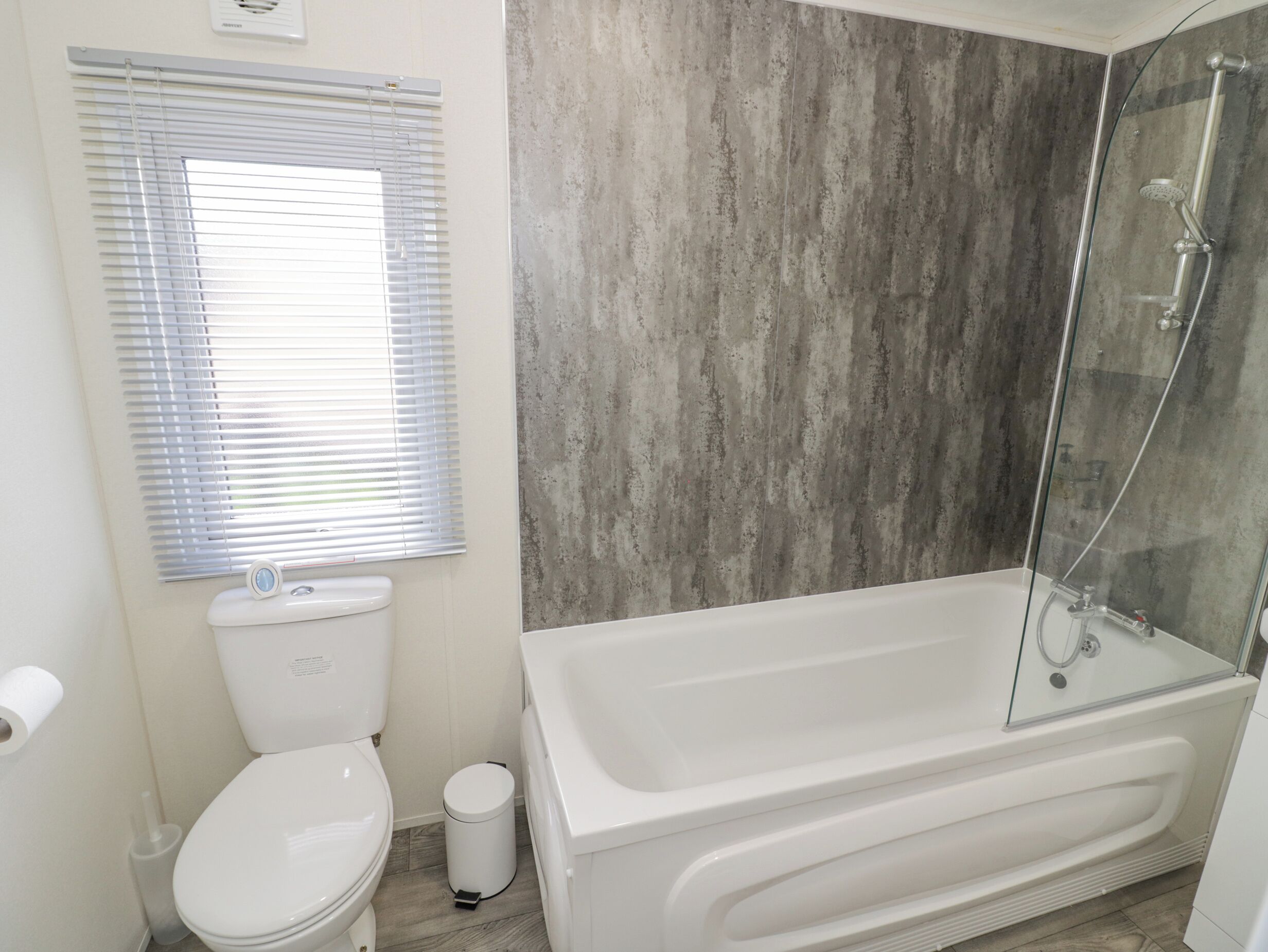 A bathroom with a toilet, a glass-enclosed shower, and a white bathtub.