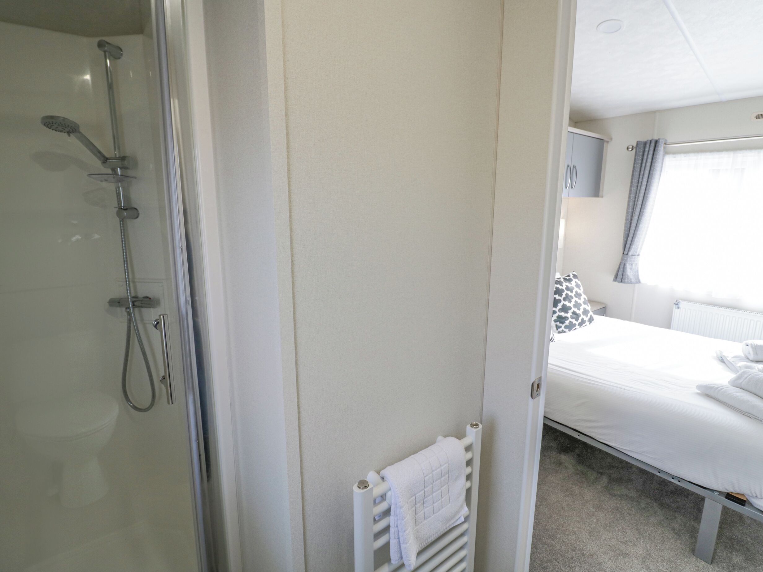 A bathroom with a shower, a toilet, and a bed with a white towel.