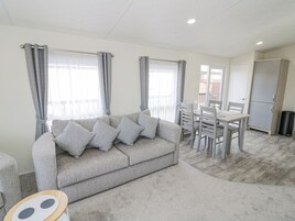 A living room with a grey sofa, a dining table with chairs, and a kitchen area with a fridge.