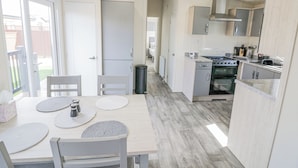 A modern kitchen with a dining area, featuring a wooden table, chairs, and a view of the backyard through a sliding door. - Long Acres Lodge (Evesham)