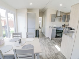A modern kitchen with a dining area, featuring a wooden table, chairs, and a view of the backyard through a sliding door.