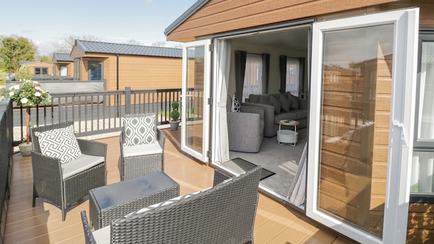 An open patio with wicker furniture, a glass door leading to a living area with sofas and a coffee table. - Long Acres Lodge (Evesham)