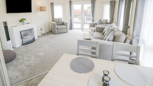 A spacious living room with a fireplace, a flat-screen TV, and a balcony with curtains. - Long Acres Lodge (Evesham)