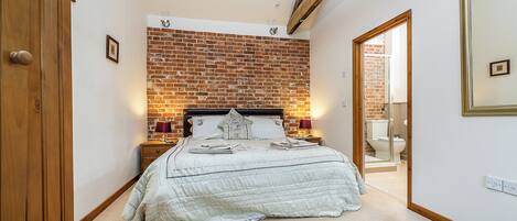 Een slaapkamer met een bakstenen muur, een bed met sprei, nachtkastjes en een spiegel.
