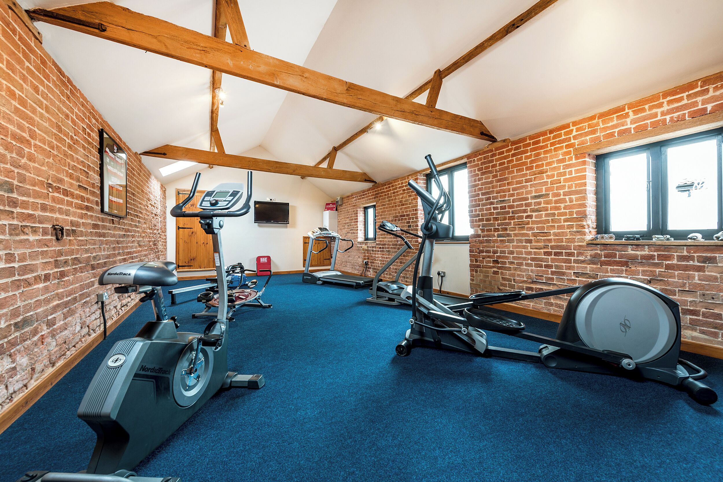 A gym with various exercise equipment, brick walls, and a high ceiling with exposed beams.