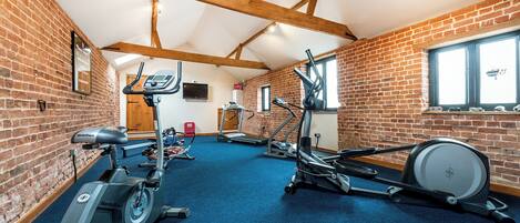 A gym with various exercise equipment, brick walls, and a high ceiling with exposed beams.