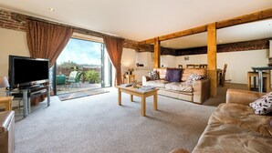 A spacious living room with a large television, a sofa, and a coffee table. There is a view of the outdoors through large windows. - Teal (Beccles)