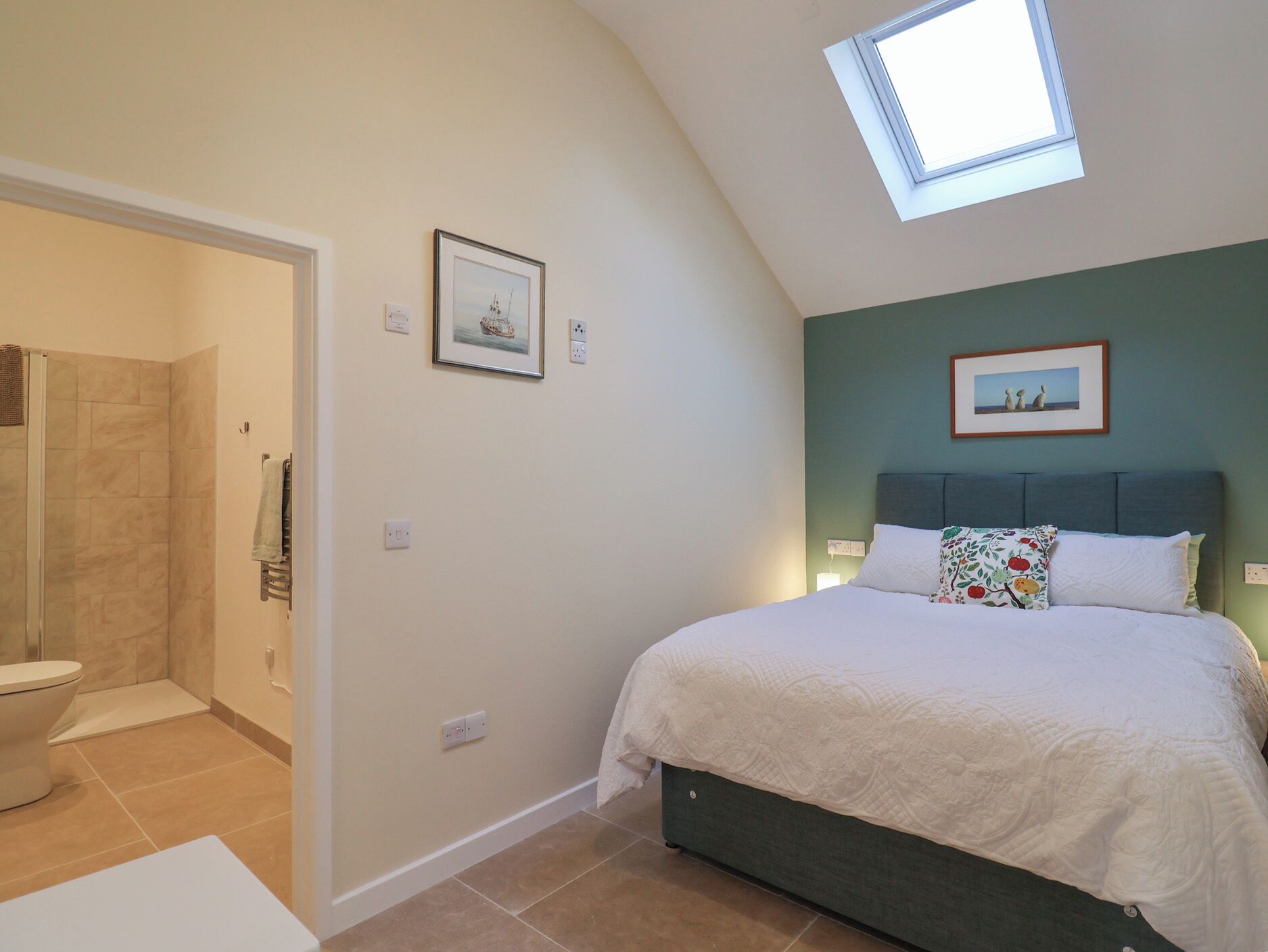 A bedroom with a skylight, a bed with a floral pillow, and a framed picture on the wall.