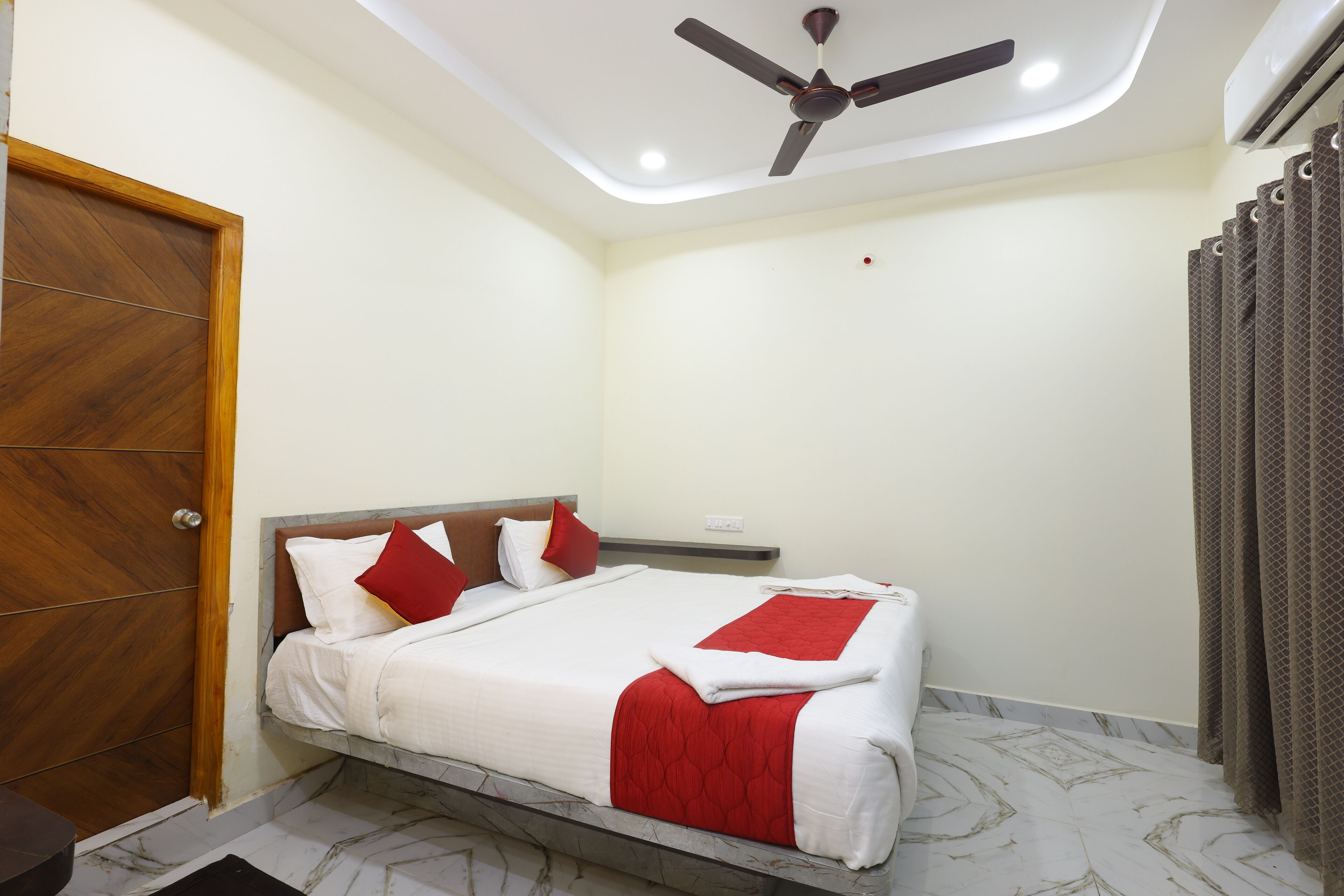 A bedroom with a bed, a ceiling fan, a wooden door, and a curtain.