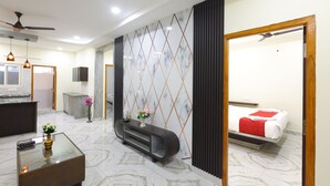 A hotel room with a bed, a small sitting area with a coffee table and a vase, a reception desk, and a view of the outside. - SBHS Homestay - Vrushabadri (Tirupati)