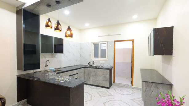 A modern kitchen with a marble island, pendant lights, and a large mirror. - SBHS Homestay - Vrushabadri (Tirupati)