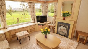 A cozy living room with a fireplace, a television, and a large window overlooking a green landscape. - Grandads Shack (Pontypool)