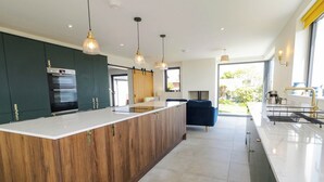 Une cuisine moderne dotée d’un îlot central, de meubles en bois, d’appareils électroménagers en acier inoxydable, de luminaires suspendus et offrant une vue sur l’extérieur.