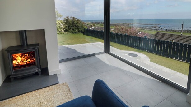 Un salon moderne doté d’une cheminée et de grandes portes vitrées donnant sur un balcon avec vue sur la mer.