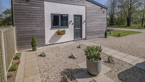 A modern building with a grey exterior, a black door, and a window. There is a small garden area with gravel, a potted plant, and a wooden fence. - Oldwyche Barns (Warwick)