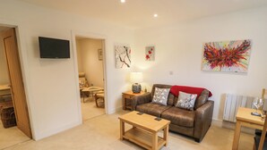 A living room with a sofa, coffee table, and a TV mounted on the wall. - Oldwyche Barns (Warwick)