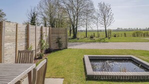 A backyard with a wooden fence, a small pond, and a grassy area with trees. - Oldwyche Barns (Warwick)