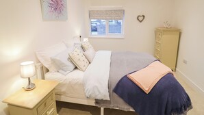 A bedroom with a bed, bedside table, lamp, dresser, window, and artwork. - Oldwyche Barns (Warwick)