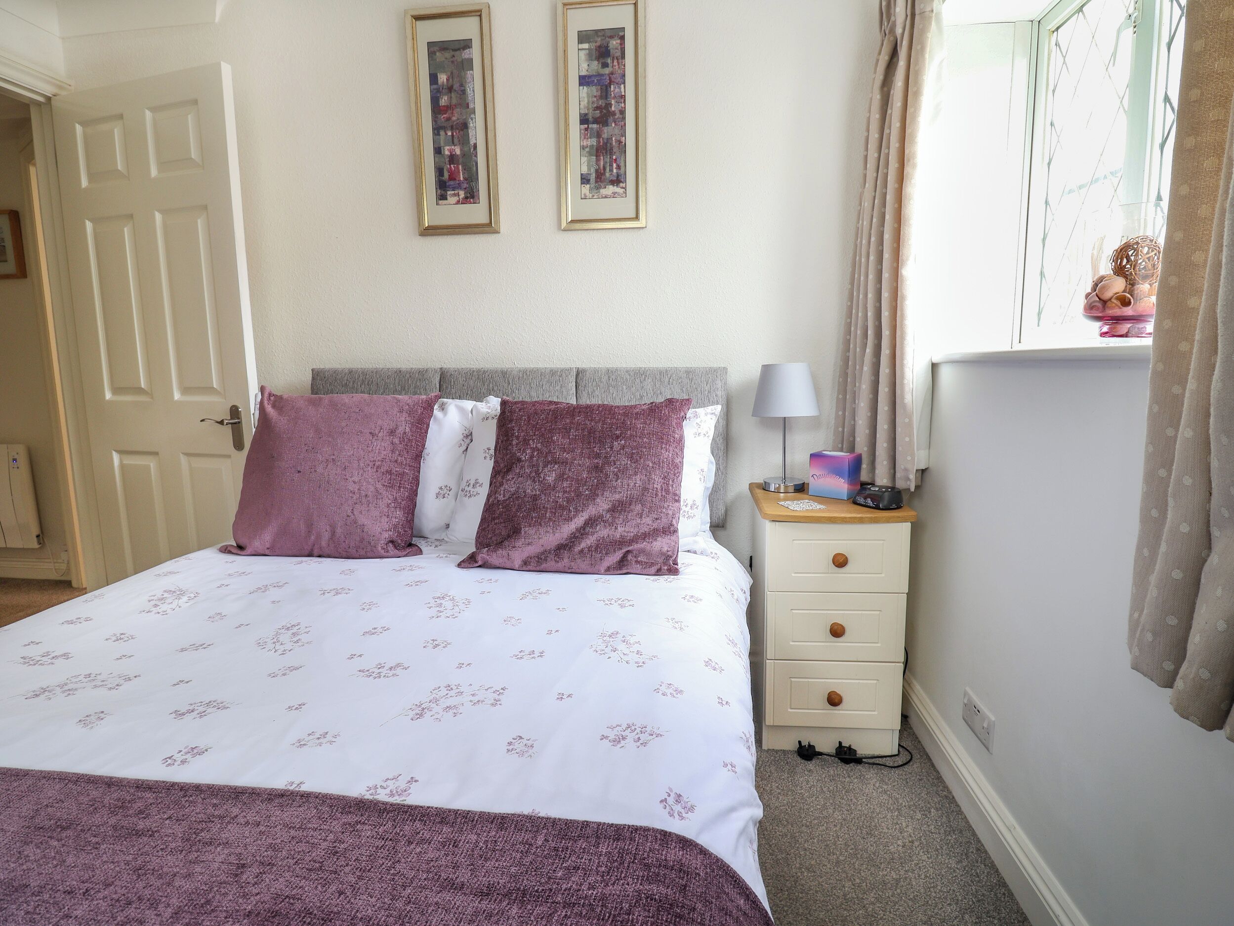 A bedroom with a bed, a nightstand, a lamp, and two framed pictures on the wall.