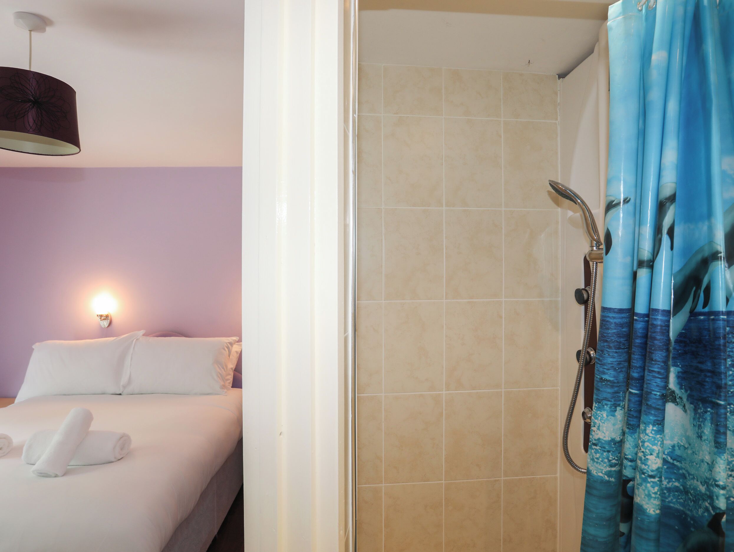 Ein Hotelzimmer mit einem Bett, einer Wandleuchte und einem Duschbereich mit blauer Duschvorhang.