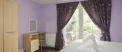 A bedroom with a bed, a wardrobe, a desk with drawers, and a window with curtains.