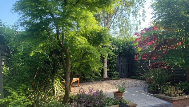 A patio with a table set for two, surrounded by lush greenery and a wooden fence. - Old Town Cottage (Stratford-upon-Avon)