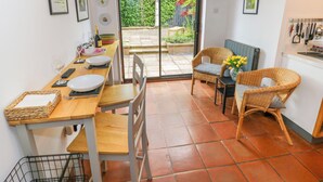 A dining area with a wooden table, chairs, and a view of the garden through a glass door. - Old Town Cottage (Stratford-upon-Avon)