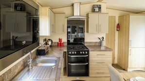 A compact kitchen with a stove, sink, and cabinets. - The Meadows 45 (Lincoln)