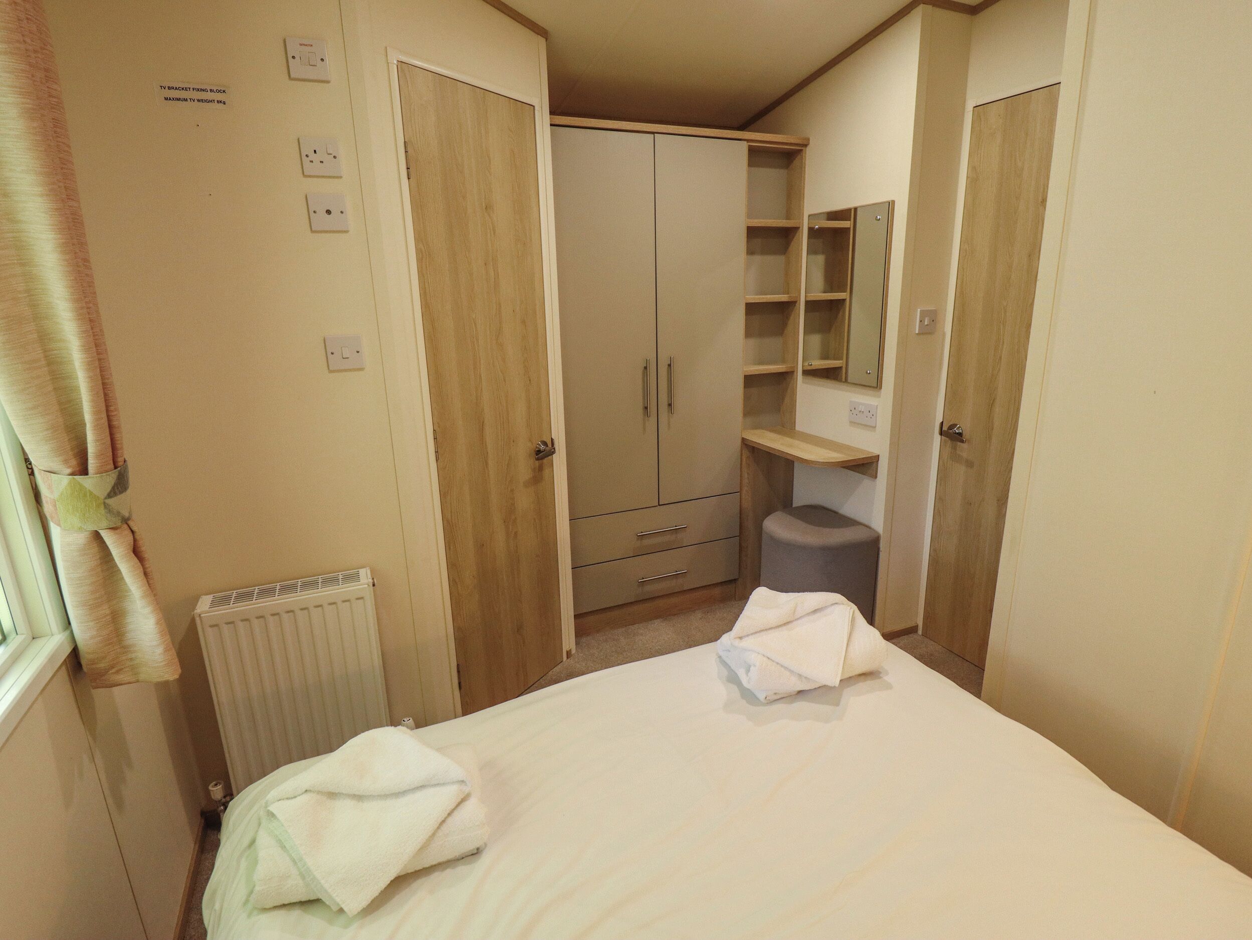 A bedroom with a bed, two bedside tables, a wardrobe, a mirror, and a radiator.