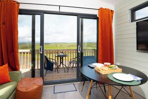 Una habitación con puerta corrediza de vidrio que da a una terraza, una mesa de comedor con una caja de comida, un sofá verde y una silla.