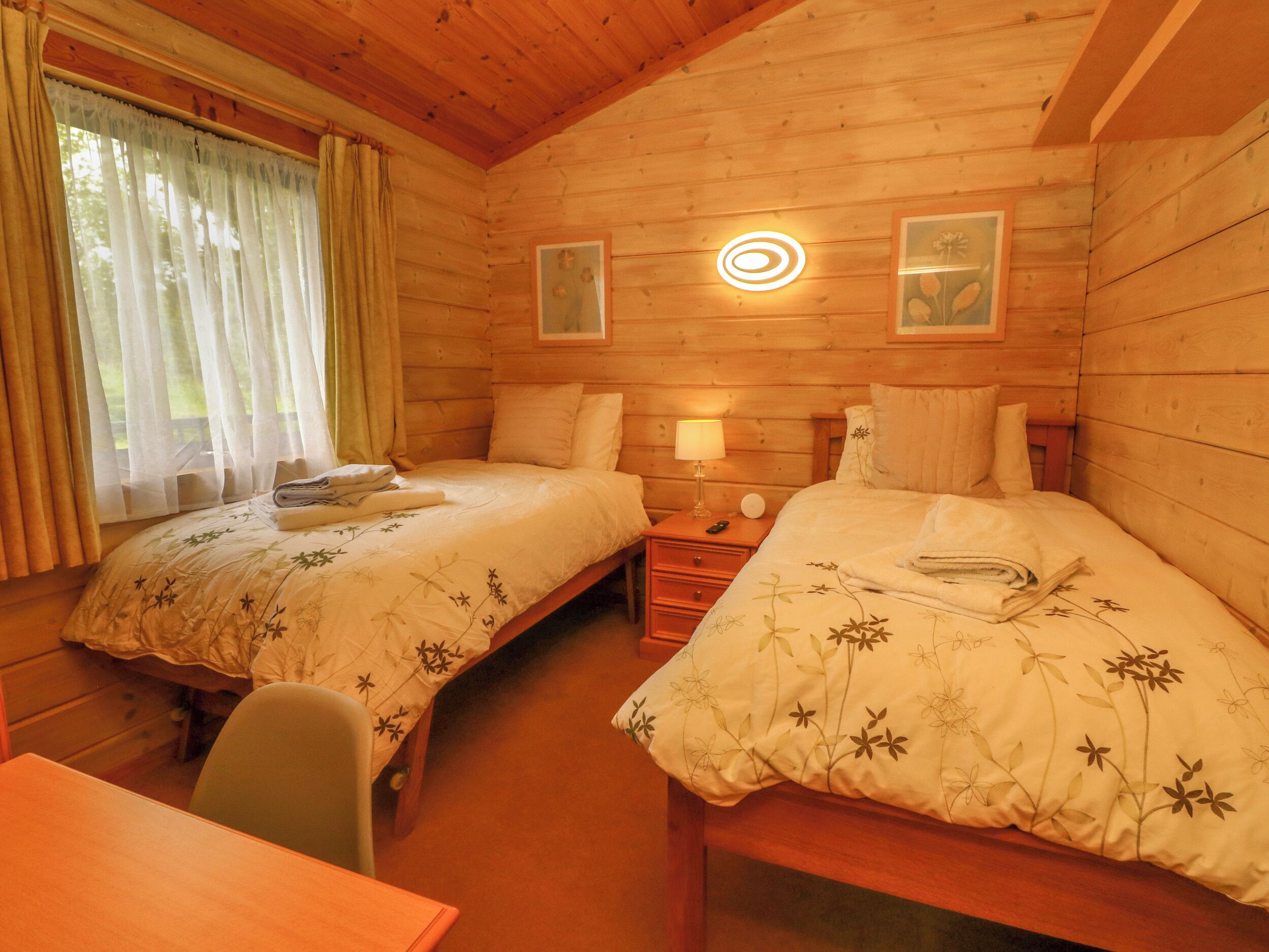 Ein gemütliches Cabin-Zimmer mit zwei Betten, einem kleinen Schreibtisch und einem Fenster mit Vorhängen.