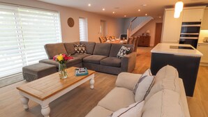 Ein modernes Wohnzimmer mit einer Eckcouch, einem Couchtisch und einem Essbereich mit einer Treppe, die zur Küche führt.