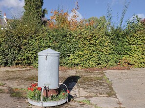 A metal utility box with a circular base, surrounded by a garden with red flowers and green foliage. - The Cart Shed (Yeovil)
