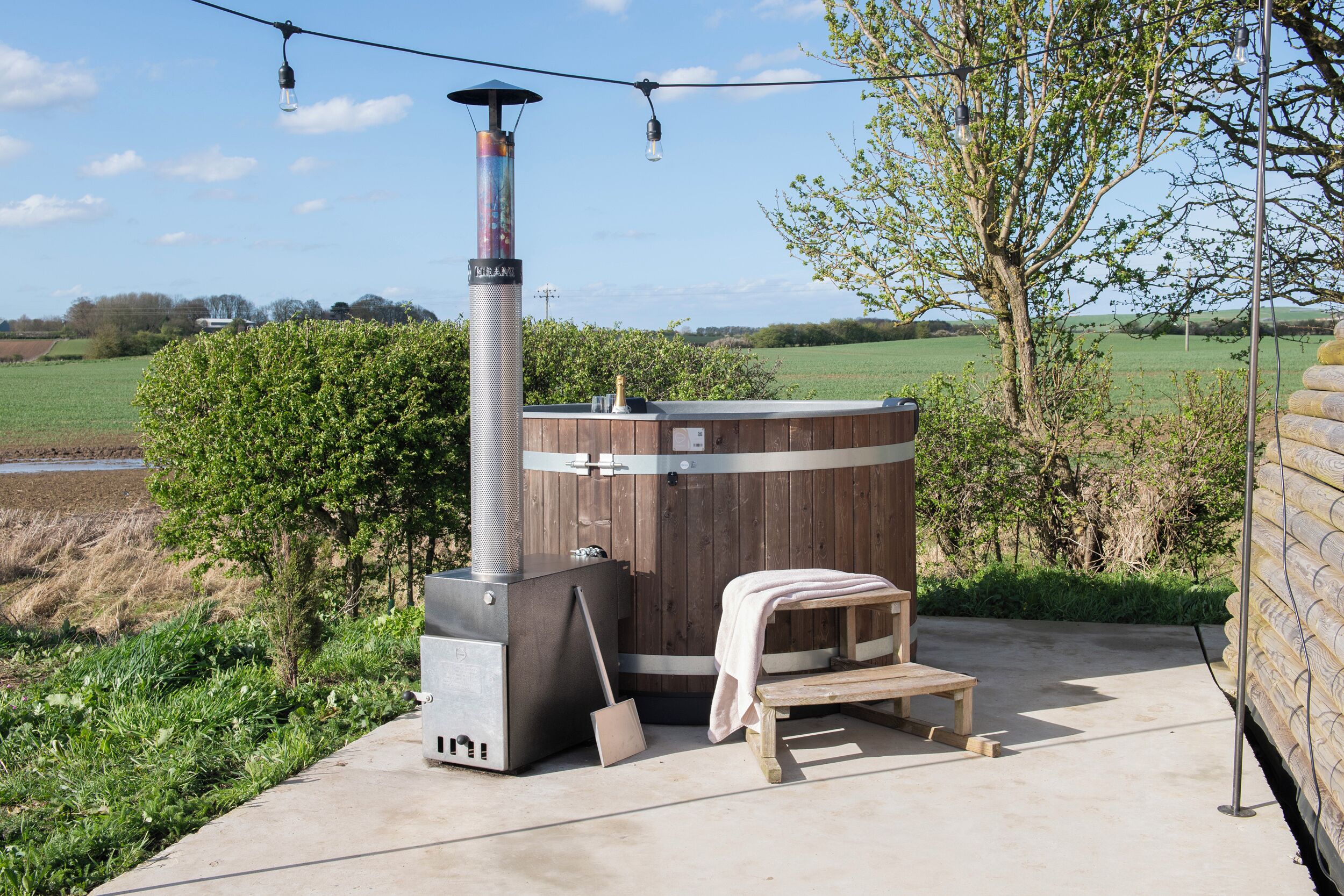 Ein Kaminofen mit Schornstein, eine Sitzbank und eine Lichterkette im Freien.