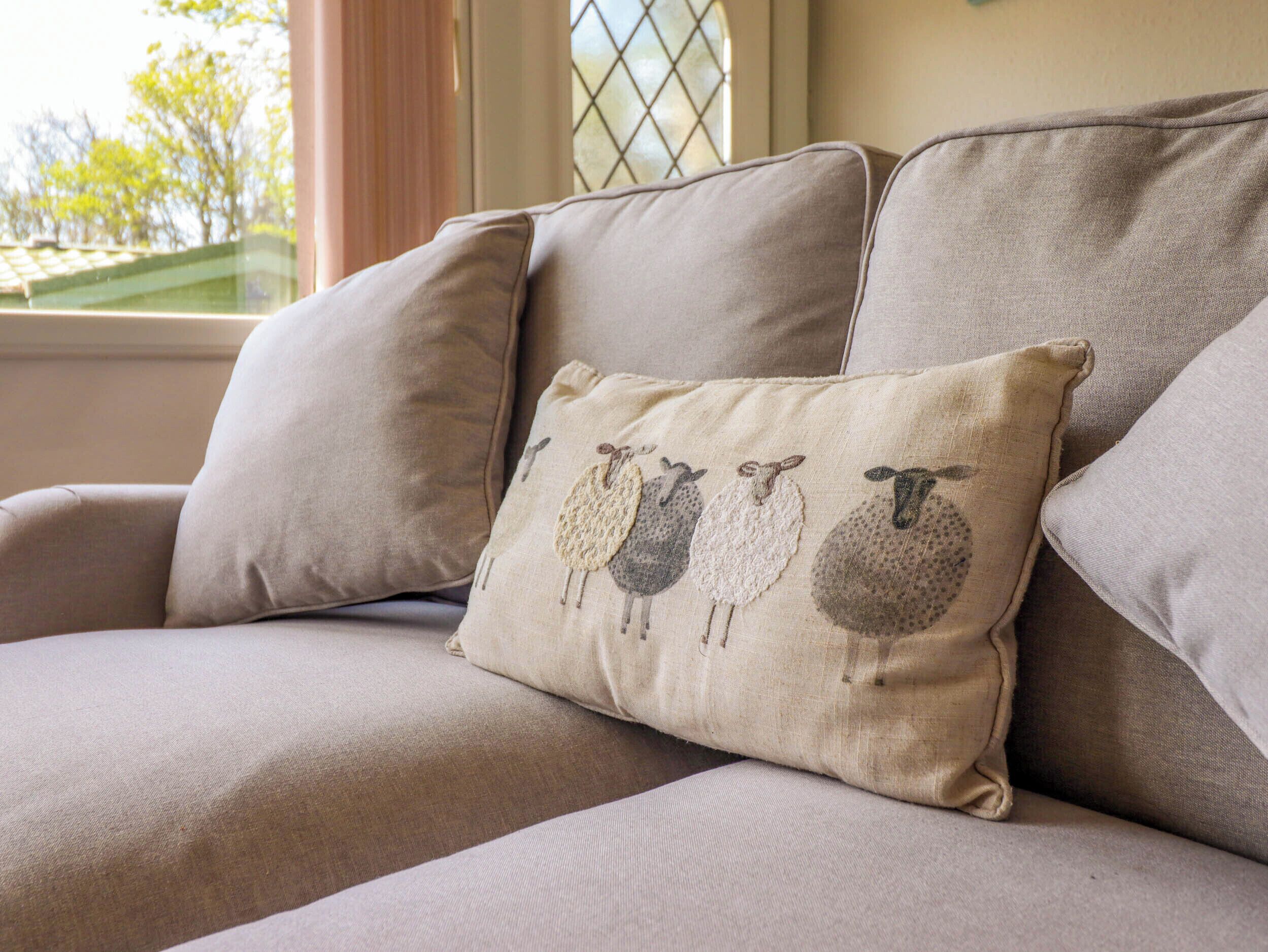 En beige sofa med en dekorativ pude med fåremotiver.