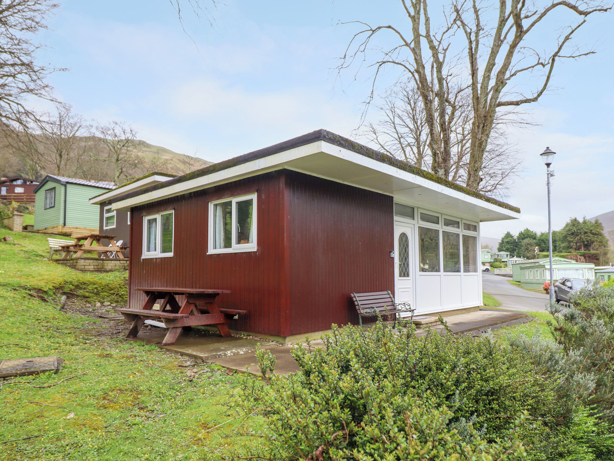 A small, single-story wooden building with a bench and picnic table outside.