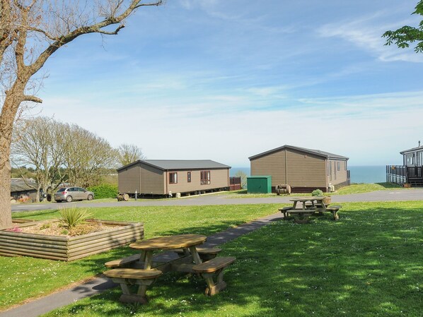 A campsite with two wooden cabins, picnic tables, and a view of the sea. - Lodge 55 at Riviera Bay Coastal Retreat (Brixham)