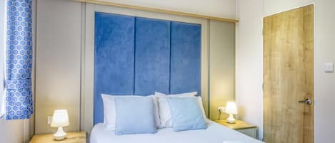A hotel room with a bed, two bedside tables, a wooden wardrobe, and a blue headboard.