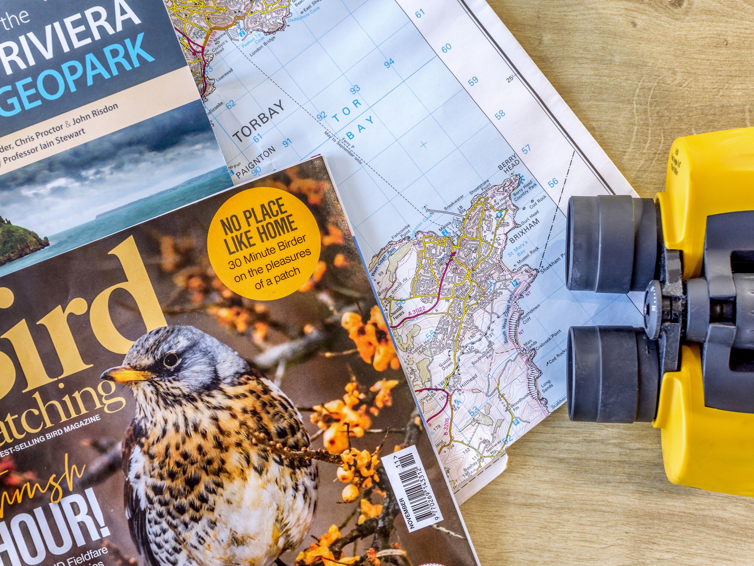 A birdwatching magazine, a map, and binoculars on a wooden surface.