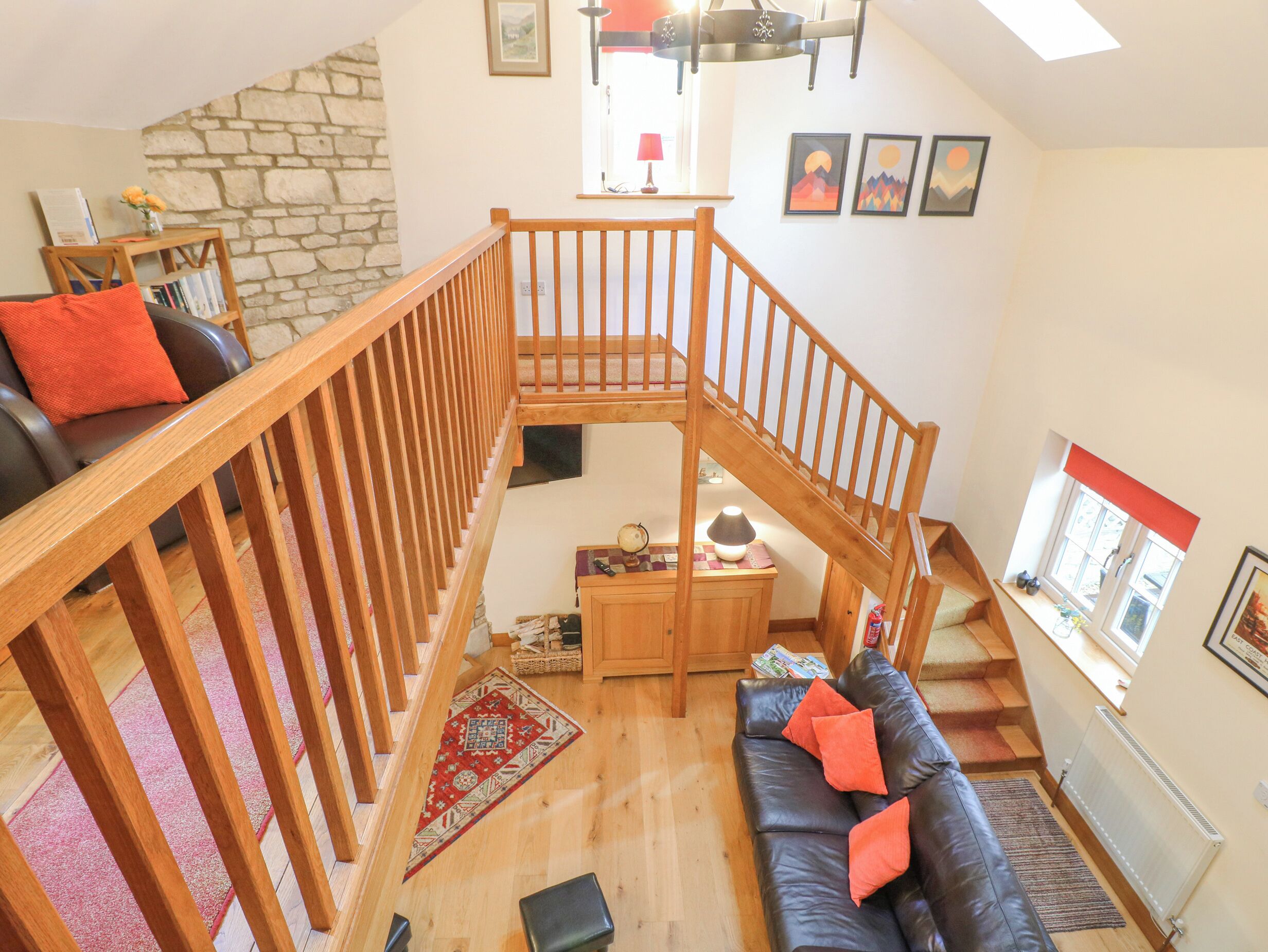 A spacious living area with a wooden staircase, a black leather sofa, and a stone wall.