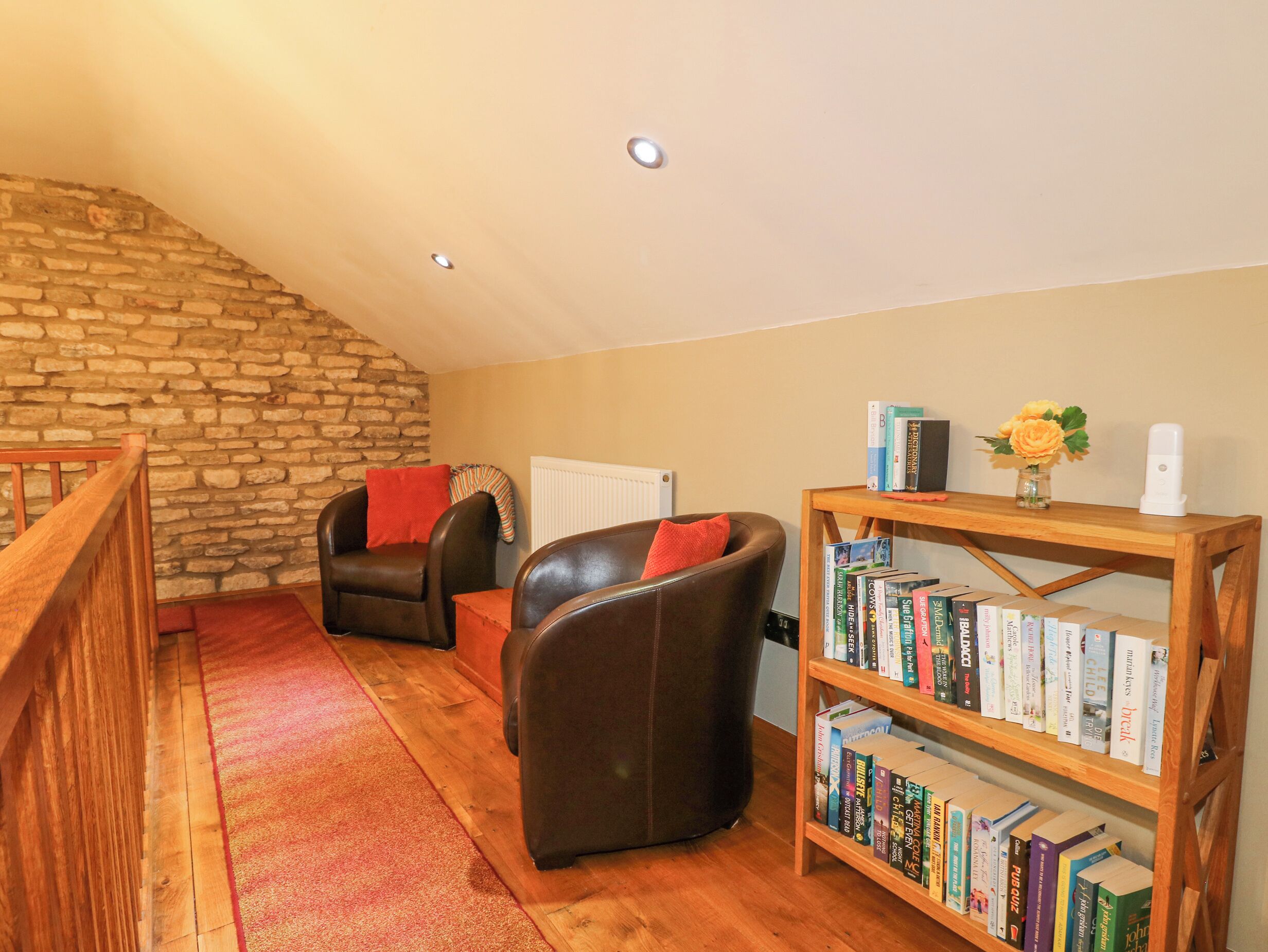 A cozy living room with a stone wall, two leather chairs, a wooden bookshelf, and a red carpet.