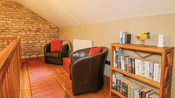 A cozy living room with a stone wall, two leather chairs, a wooden bookshelf, and a red carpet.