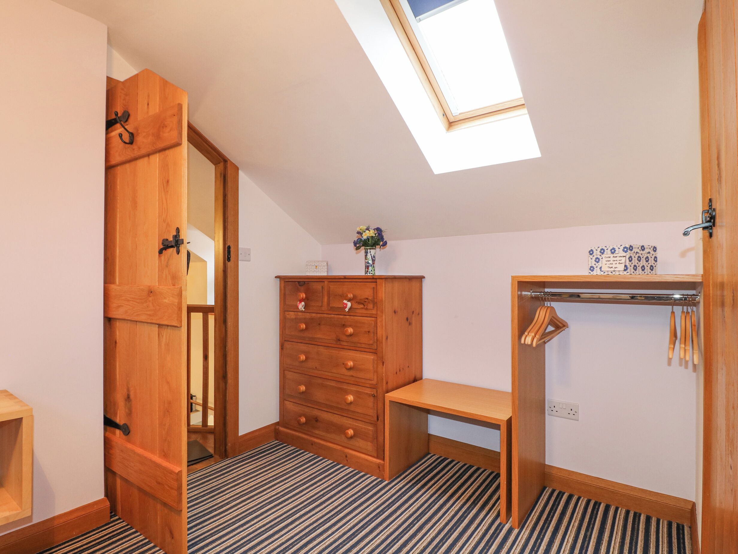 A room with a skylight, wooden wardrobe, a small table, and a coat rack.