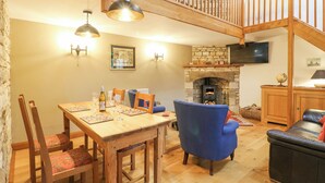 Un comedor con una mesa y sillas de madera, un sillón azul, una chimenea y un televisor montado en la pared.
